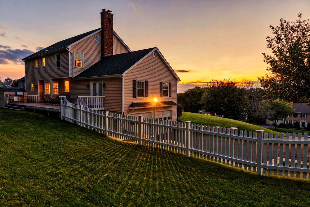 A close up of a residential property at sunset with a white fence encircling the perimeter.